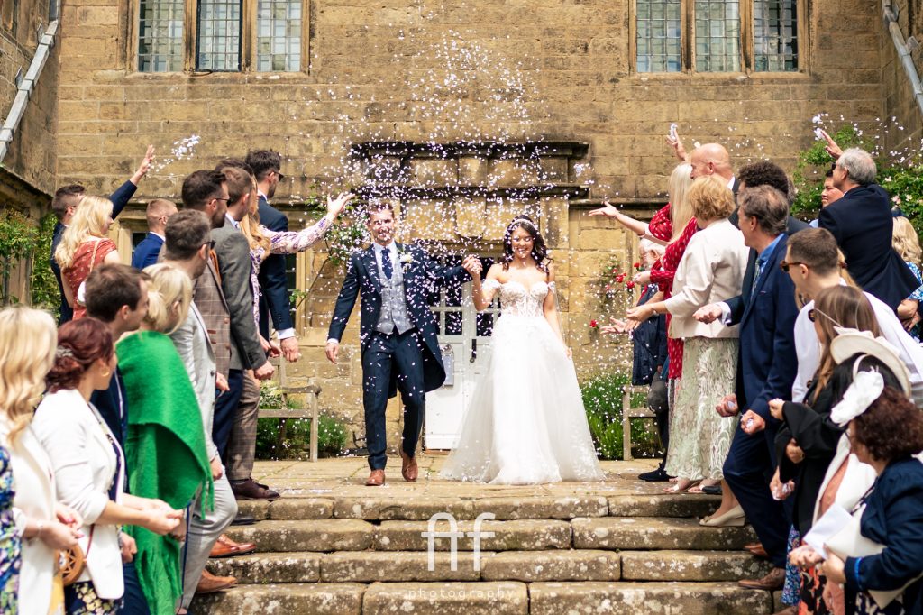 Bride and Groom exiting from a Peak District wedding venue with all their guests throwing confetti