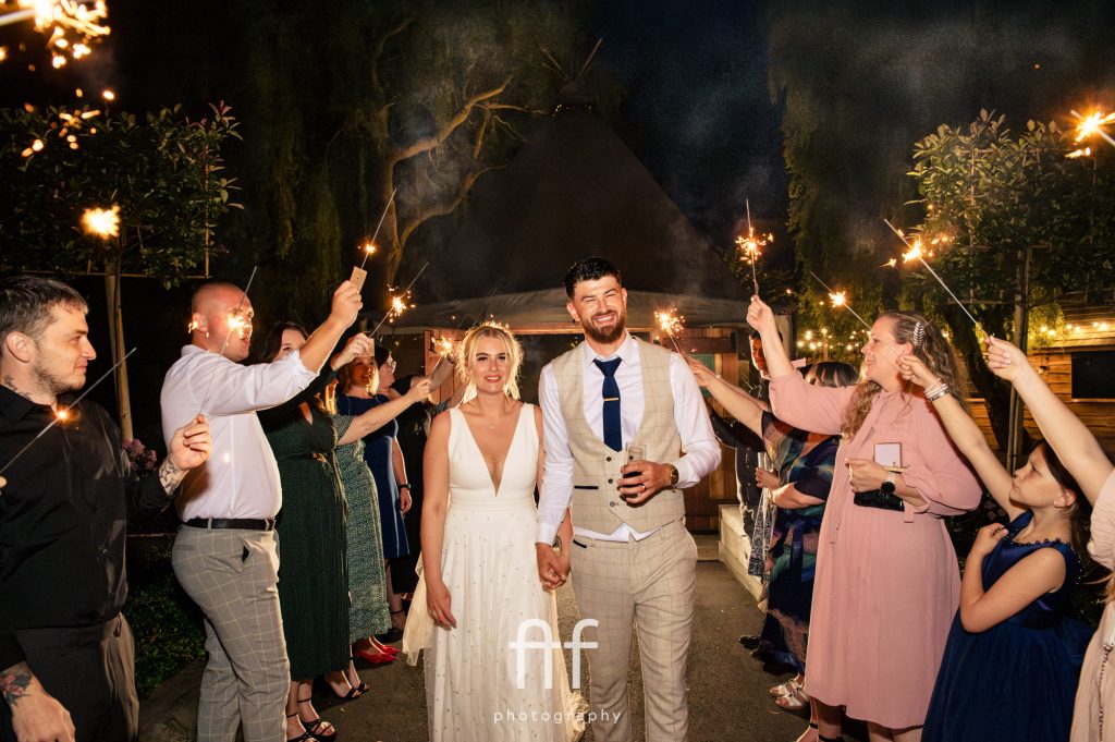 Bride and groom walking through their guests who are shining sparklers and having fun